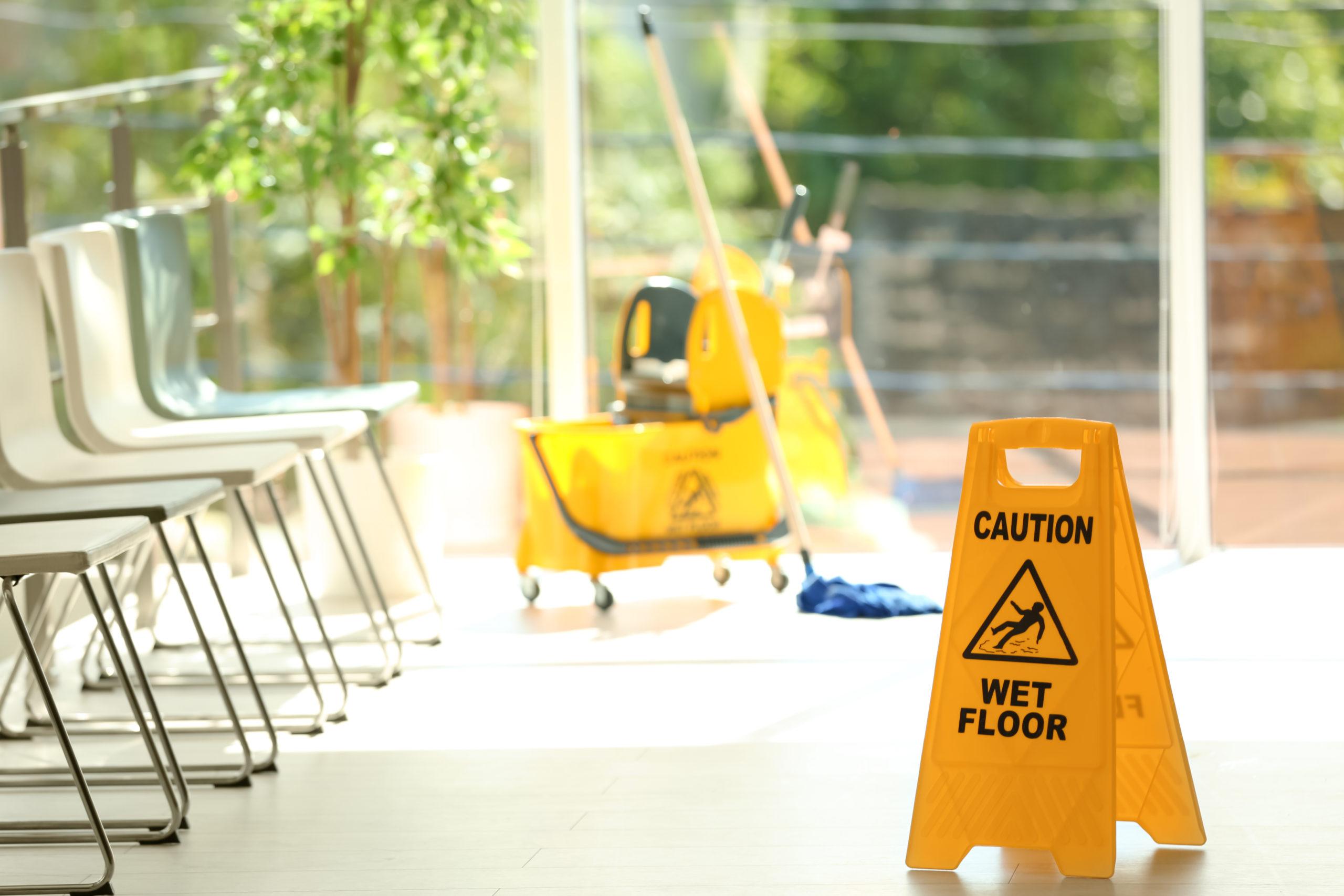 a waiting room with chairs down the left hand side, a mop and mop bucket in the background, and a caution wet floor sign in the foreground