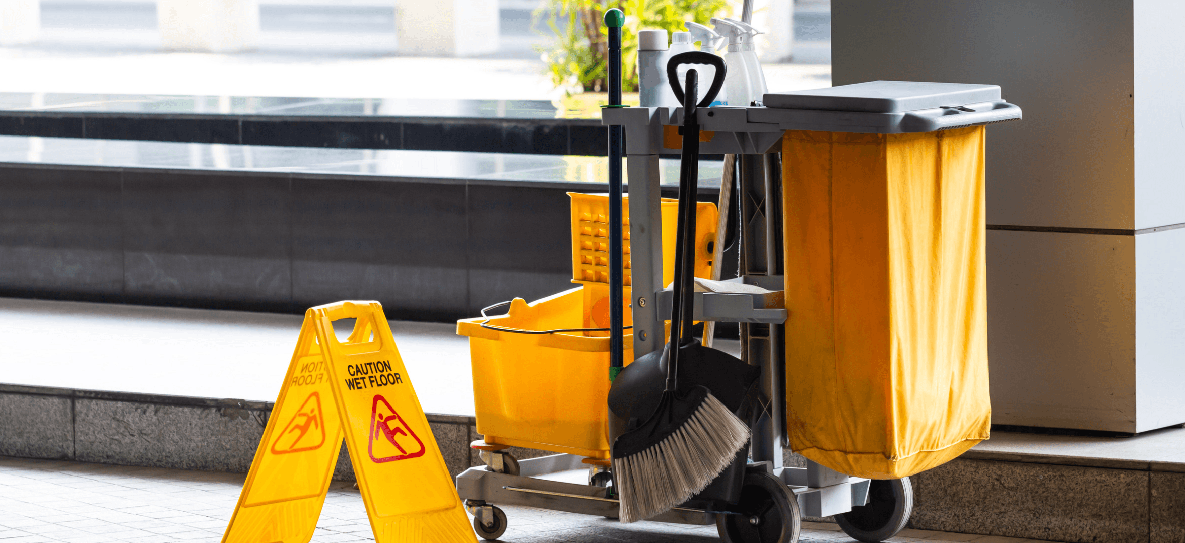 A cleaning cart in front of a large window with a caution wet floor sign.